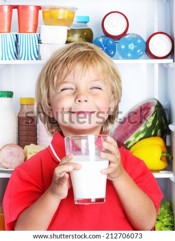 Happy little boy with milk against refrigerator with food