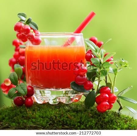 Berry juice and forest cowberry with leaves against blurred green background.