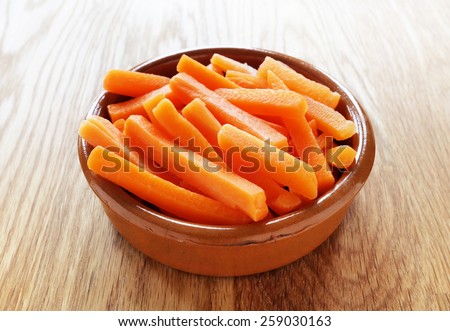Raw carrot sticks in brown rustic bowl on wooden table