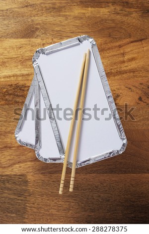 Pile of three silver foil takeaway trays with chopsticks placed on top shot on wooden table top