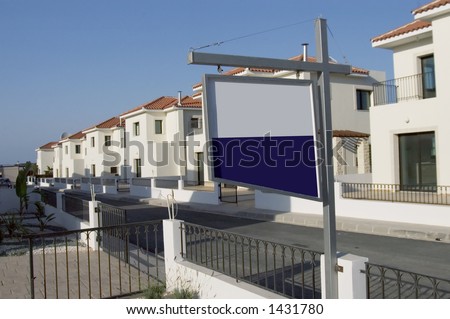 New development of European villas with a blank for sale board in the foreground