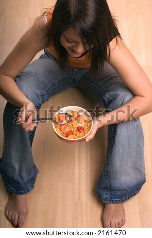 Young woman sat eating a bowl of corn flakes cereal with strawberries on top.