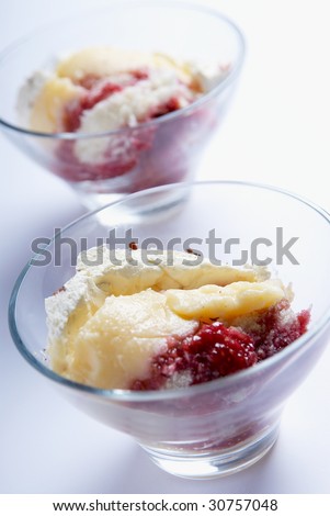 Two trifle portions in glass bowls, made with raspberries,custard,sponge,whipped cream and grated dark chocolate