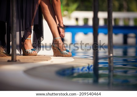 beautiful legs in blue shoes of a young girl near the blue water in swimming pool
