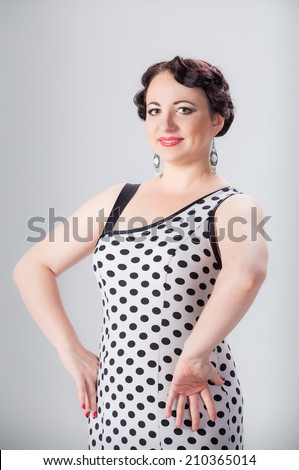 young beautiful brunette female spanish flamenco dancer in black and white flamenco dress posing with arms on her hips in studio on gray background