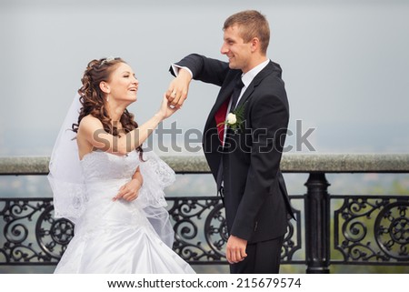 beautiful brunette bride in white wedding dress and young handsome groom in black suit dance on big city background