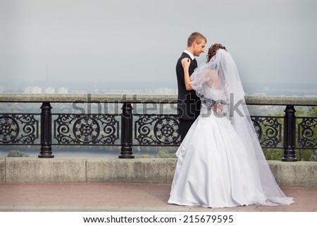 young handsome groom dance with his beautiful brunette bride in white wedding dress on big city background