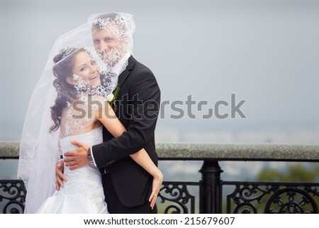 beautiful brunette bride in white wedding dress and young handsome groom in black suit stand on big city background