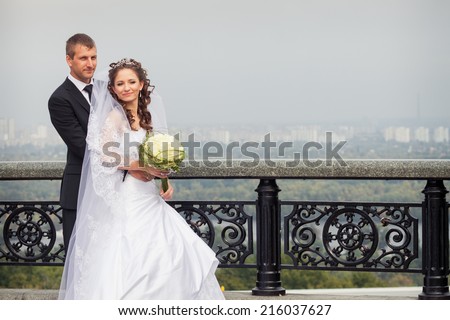 young handsome groom hold his beautiful brunette bride in white wedding dress on big city background