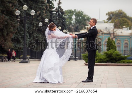 young handsome groom in black suit dance with his beautiful brunette bride in white wedding dress on big city background