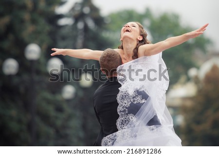 young handsome groom in black suit hold his beautiful brunette bride in white wedding dress on big city background