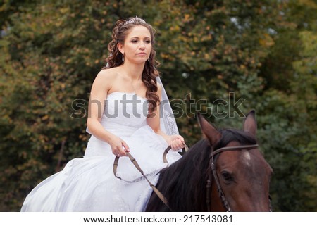 young charming brunette bride in white wedding dress and tracery veil rides on horse