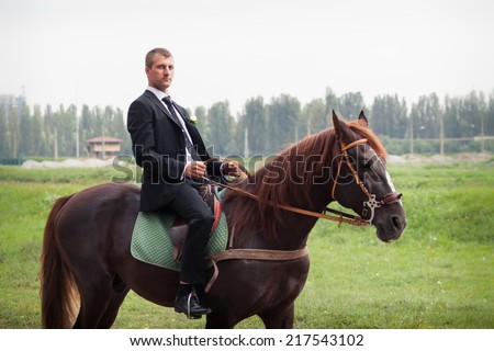 handsome young in black suit groom rides on horse