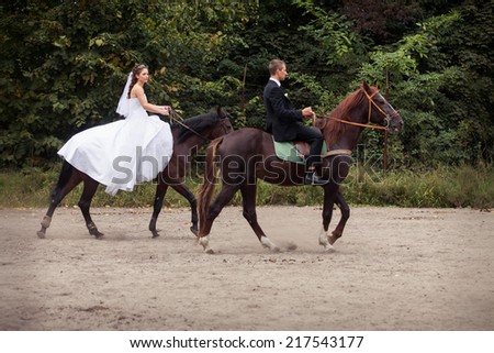 young charming brunette bride in white wedding dress and handsome groom in black suit rides on horses