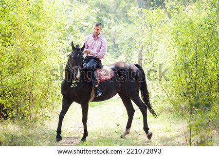 handsome man in pink shirt ride on the black horse in green forest
