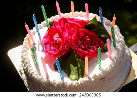 closeup white creamy delicious cake decorated with candles  and three red roses on the top