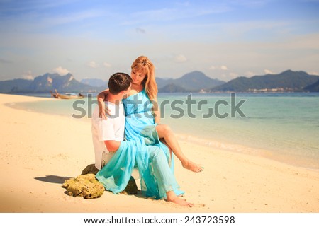 handsome man hold on his knees beautiful blonde woman in elegant dress with blue sea and mountains on background