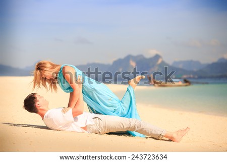 handsome man hold on his hands beautiful blonde woman in elegant dress with blue sea and mountains on background