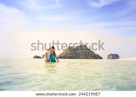 handsome man hold his beautiful blonde wife in elegant dress stand in water with green mountain on background