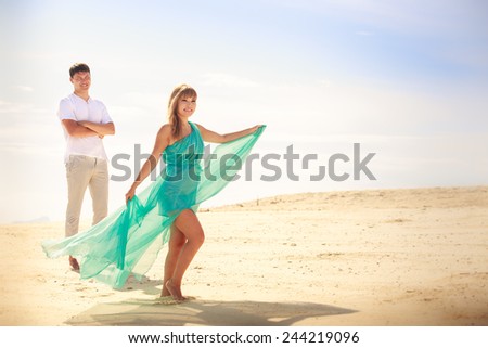handsome man look on his beautiful blonde wife in elegant dress on island beach