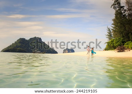handsome man run with his beautiful blonde wife in elegant dress on island beach with green mountain on background