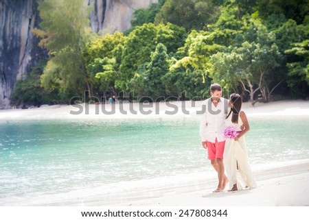 handsome groom walk with pretty brunette bride in long white wedding dress on island beach white sand in Thailand