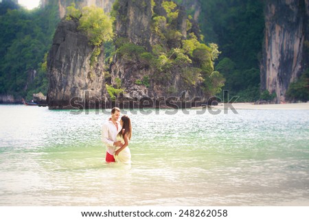 brunette girl with handsome man stand in sea water in island bay with green mountain background