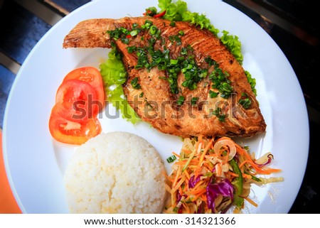 view of fried fish with rice and vegetables on white big plate on table