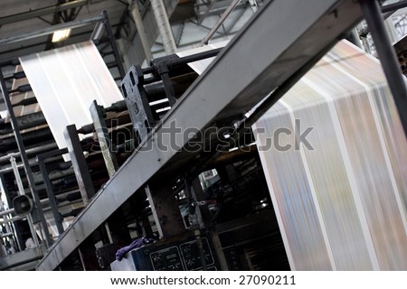 A large offset printing press running a long roll off paper over its rollers at high speed.