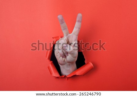 Make a victory sign by use his hands through hole on the red paper.