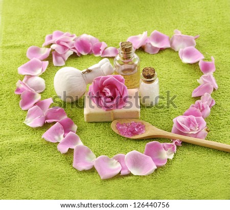 Heart pink rose petals with towel, soap, massage oil, salt in spoon on towel