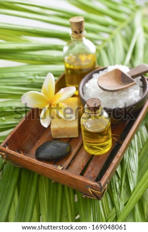 spa supplies with frangipani. salt in bowl, oil, stone onpalm background