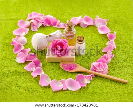 Heart pink rose petals with towel, soap, massage oil, salt in spoon on towel
