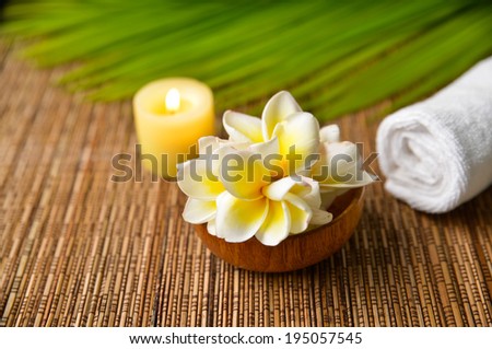 Spa sitting with candle ,green palm, towel , frangipani in bowl on mat