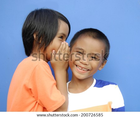 One little girl whispering to other some news. Surprised face and palm near face in second little boy-blue background