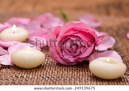 pink rose and petals with three white candle on mat