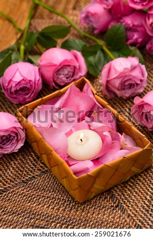 rose and petals with white candle in basket on mat