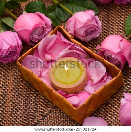 rose and petals with white candle in basket on mat