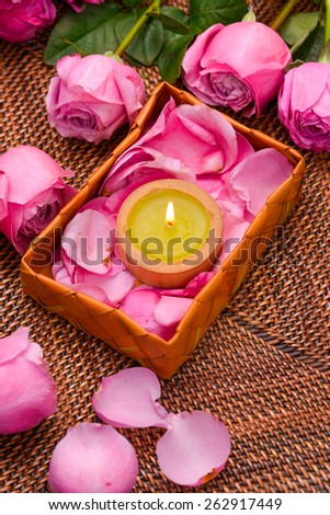 Pink rose and petals with white candle in basket on mat
