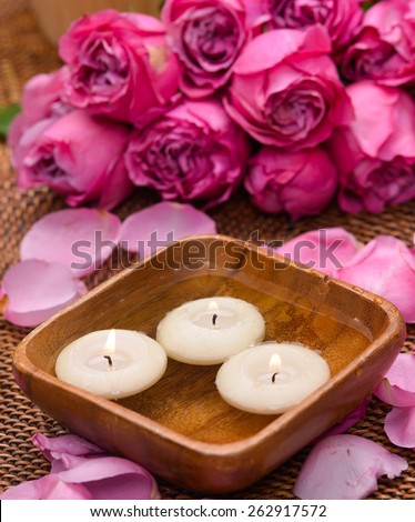Set of rose and petals with white candle in bowl on mat
