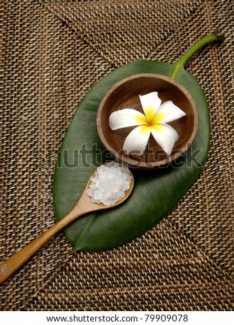 frangipani flower in bowl and herbal salt in spoon with leaf on burlap texture mat
