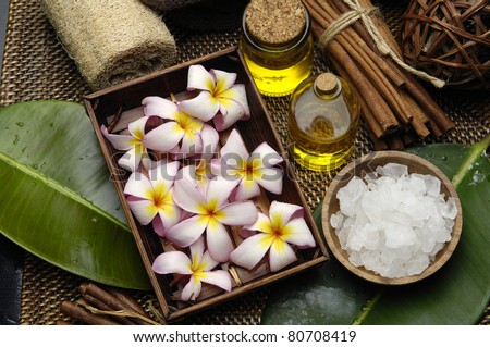 Spa wellness products Ã¢Â?Â? many frangipani in wicker basket with massage oil and salt on bowl and  green leaf on burlap mat