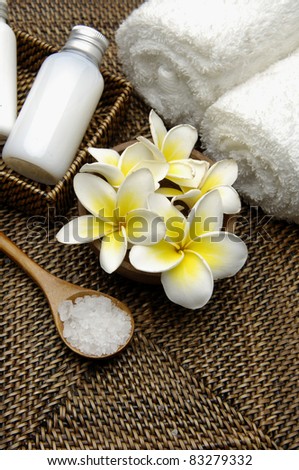 herbal salt in spoon and roller towel with massage oil and frangipani on mat