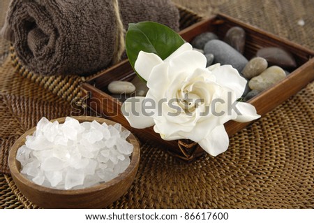 spa salt in bowl and gardenia flower and stones on burlap texture