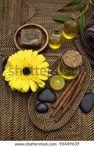 Candle with massage oil and stone in bowl and with yellow gerbera on burlap texture
