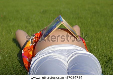 pregnant woman lying on the grass with the small book on the belly