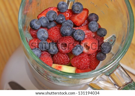 Fruit, including blueberries, raspberries, strawberries and pineapple, in a blender, about to made into a smoothie.
