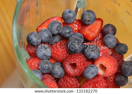 Fruit, including blueberries, raspberries, and strawberries, in a blender, about to made into a smoothie.