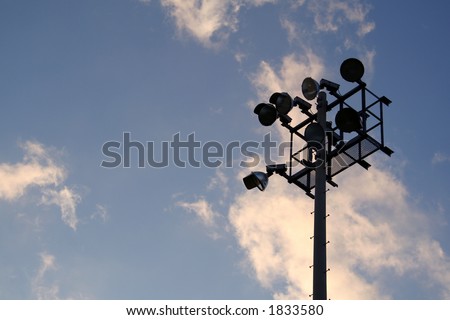 The silhouette of stadium light stand set against a blue sky with white clouds.