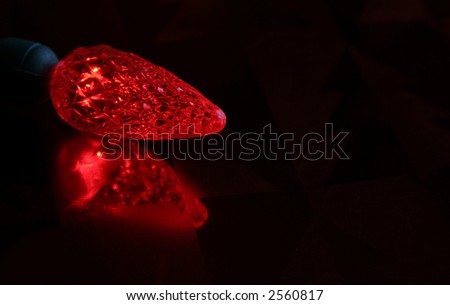 A single red led christmas light resting on a glossy red background.